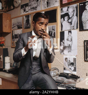 Sammy Davis Jr. 1925-1990. American singer, musician, dancer, actor. Pictured here in his office. On the wall behind him, pictures of his swedish wife May Britt Wilkens and their children. 1963 Stock Photo