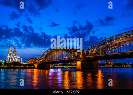 Cologne, Germany: Beautiful night landscape of the gothic cathedral, Hohenzollern Bridge and reflections over the River Rhine with clouded empty sky f Stock Photo