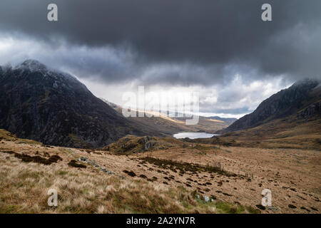 Hikers in Ogwen Valley Winter landscape with snowcapped Pen Yr Ole Wen and Tryfan mountains with dramatic light Stock Photo
