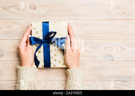 Female hands holding present on yellow rustic wooden background. Festive backdrop for Christmas holidays or other holiday . Flat lay style top view wi Stock Photo
