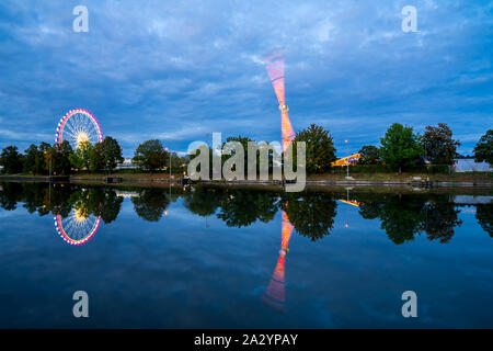 Germany, Colorful illuminated big wheel and lights of giant swabian fair called cannstatter wasen in stuttgart city in evening twilight reflected in n Stock Photo