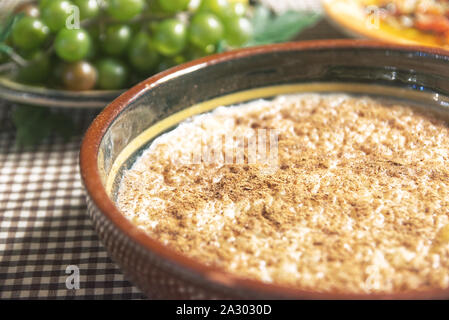 Typical Spanish arroz con leche, rice pudding on a table covered by a tablecloth served with some fruits and in a rustic kitchen. Empty copy space. Stock Photo