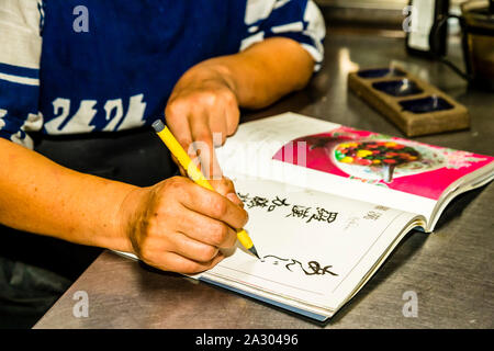 Rakan, a kaiseki restaurant run by chef Atsuko Kato, on the Izu Peninsula, Japan. Atsuko Kato's hands guide the brush pen as she writes the calligraphic dedication in her book. Stock Photo
