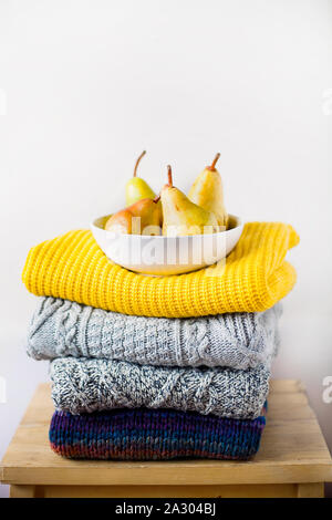Stack or pile of fashionable knitted colors wool clothes or sweaters with different knitting patterns on wooden chair and a white wall with copy space Stock Photo
