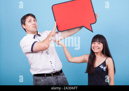 Asian girlfriend pointing at his caucasian boyfriend while he is holding an empty sign. Interracial couple. Stock Photo