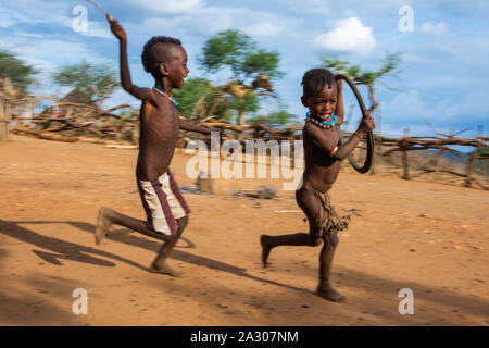 Turmi, Ethiopia - Nov 2018: Hamer tribe kids playing with the tire. One chasing another one. Omo valley Stock Photo