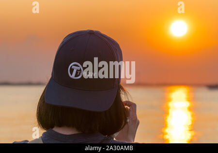 Long Island, NY - Circa 2019: Female photographer taking pictures of beautiful orange sunset using Tiffen brand glass lens filters to create dramatic Stock Photo