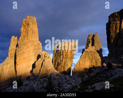 Pale greyish rock formation of Cinque Torri turning red on a background of dark clouds at sunset. Cortina d'Ampezzo, Dolomites, Veneto, Italy. Stock Photo