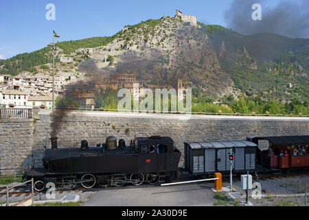 AERIAL VIEW from a 6-meter mast. Historic steam train leaving Entrevaux Station with the city fortification at the clifftop. Entrevaux, France. Stock Photo