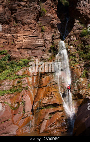 Young man abseiling a waterfall in a red rock formation. Clue d'Amen, Gorges de Daluis, Guillaumes, Alpes-Maritimes, France. Stock Photo