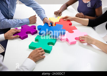 Hands Of Businesspeople Building Colorful Jig Saw Puzzles Together Over White Desk At Workplace Stock Photo