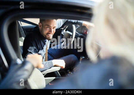 Happy Young Man Looking At His Female Friend Standing Outside The Car Stock Photo