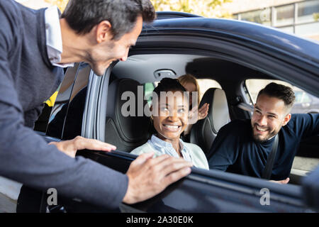 Smiling Man Looking At His Cheerful Young Friends Sitting Inside Car Through Window Stock Photo