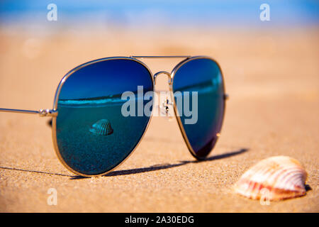 Mirror sunglasses on the summer tropical beach, the shell and stormy sea are reflected in the mirror sunglasses, summer concept photo Stock Photo