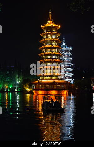 Beautiful floating Sun and Moon pagodas of Guilin water reflected in park lake at night and leisure boat silhouetted in romantic scene, China Stock Photo