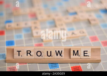 The Dutch word 'trouw me' (in English: 'marry me') in wooden scrabble tiles on a rack. The background a vintage board, out of focus, with copy space Stock Photo