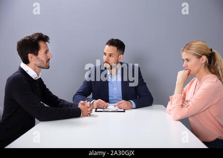 Male Investment Adviser Or Lawyer Looking At Young Couple Seating In The Office Stock Photo