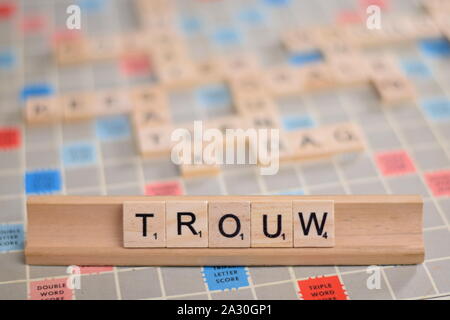 The Dutch word 'trouw' (in English: 'faithful') in wooden scrabble tiles on a rack. The background a vintage board, out of focus, with copy space Stock Photo