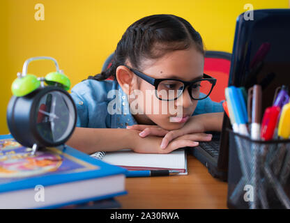 Cute girl wearing glasses is searching for information on internet from laptop on the desk isolated yellow background, Education concept. Stock Photo