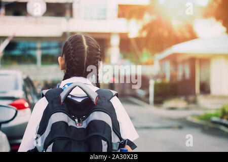 Little girl walking into school with backpack in the morning under warm sunshine. Education concept. Stock Photo