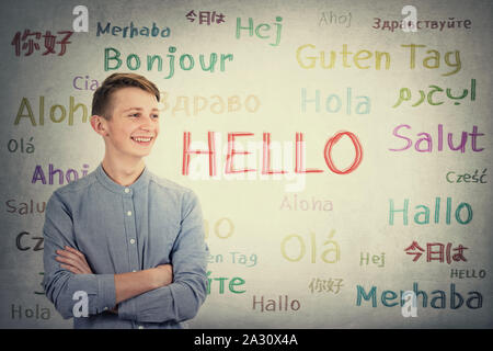 Positive boy adolescent keeps arms crossed looking aside tooth smile over grey wall background written with the word hello in different languages and