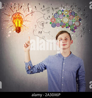 Casual teen boy pointing his index finger up showing a bright light bulb on the wall. Idea concept, positive thinking as colorful gear brain above hea Stock Photo