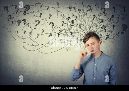 Thoughtful stressed teenage boy pointing finger to forehead feel discomfort. Hard thinking, anxiety and headache, mental health problem concept. Stock Photo