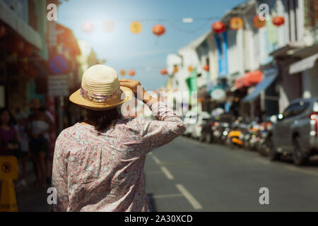 Woman traveler in casual dress walking in thalang road with chino portuguese style building under sunlight view from behind. Phuket, Thailand Stock Photo