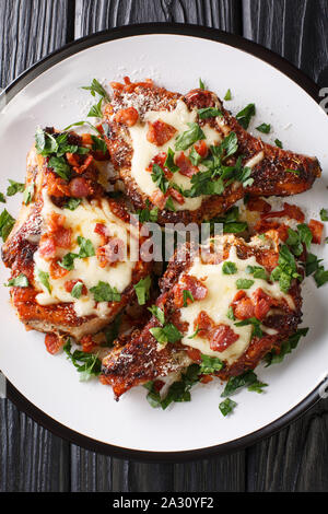 Baked pork chops with cheese and bacon closeup on a plate on the table. Vertical top view from above Stock Photo