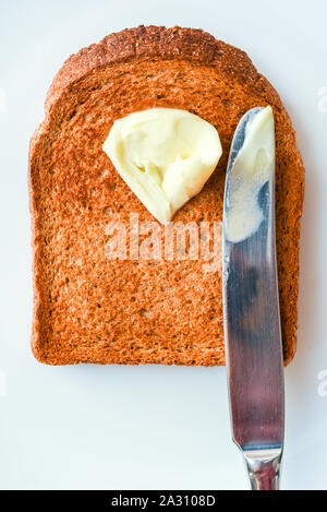 Slice of hot toast with melting butter and knife on a white plate Stock Photo