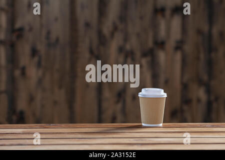 A cardboard cup for take away drinks standing on the wooden table on a wooden background Stock Photo
