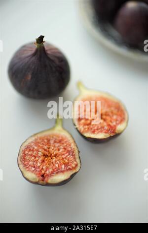 One whole fig and the second cut in half lie on a white table. Stock Photo