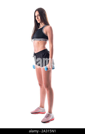 Beautiful, woman stands in sportswear. Tight, athletic body, thin, flat  stomach. Holding dumbbells in his hands. Download biceps, chest muscles.  Drying. Do fitness. White background, isolate. фотография Stock