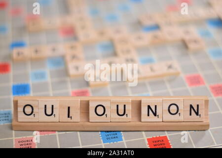 The French words 'oui ou non' (in English: 'yes or no') in wooden scrabble tiles on a rack. The background a vintage board, out of focus, copy space Stock Photo