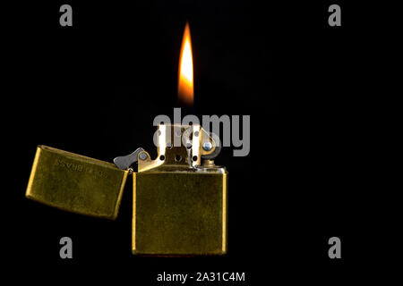 Well used brass lighter with flame isolated against a black background Stock Photo