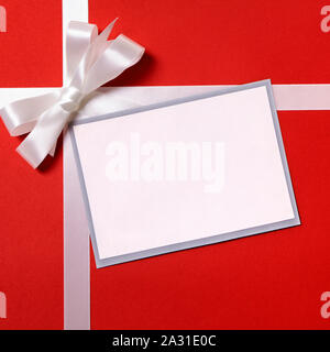 Christmas gift card or label and envelope, white ribbon bow, red wrapping paper background, copy space Stock Photo