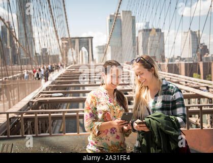 Two twenty year old female tourists compare cell phone photos on the Brooklyn Bridge in New York City, USA. Stock Photo