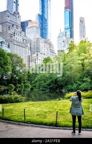 Young woman tourist photographs pond and buildings in Central Park, New York City, USA. Stock Photo