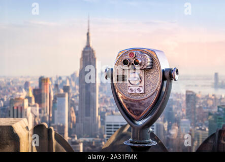 One of the iconic telescopes on Top of the Rock Observatory with the Empire State Building in the distance, New York City, USA.