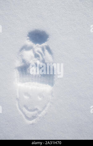 The figure of the face and imprint of the cap on white snow, a sunny frosty day. Close-up. Stock Photo