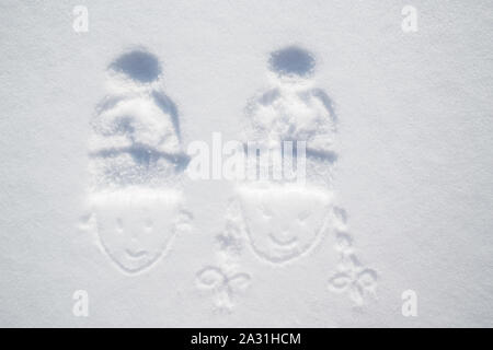 Drawing faces of a boy and girl with the imprint of hats on his head against the white snow, frosty sunny day. Close-up. Stock Photo