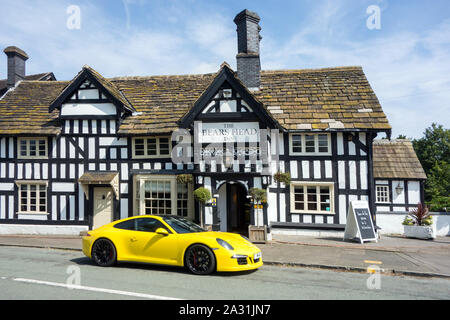 Yellow Porsche sports car parked outside a traditional English black and white half timbered inn public house at Brereton Cheshire England