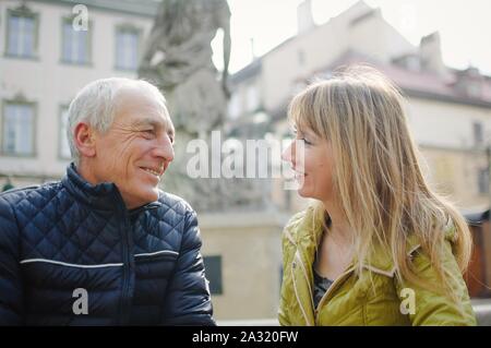 Handsome elderly man is embracing his young blonde wife spending time together outdoors in the ancient city during early spring or autumn. Stock Photo