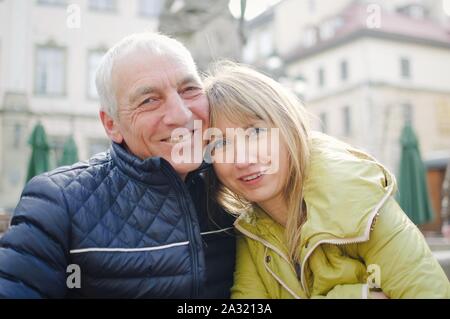 Handsome elderly man is embracing his young blonde wife spending time together outdoors in the ancient city during early spring or autumn.