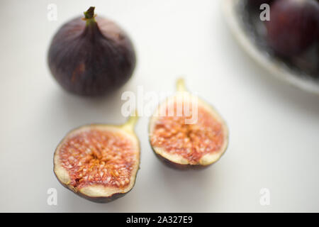 One whole fig and the second cut in half on a white table Stock Photo