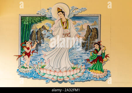 Si Racha, Thailand - March 16, 2019: Closeup of Painting of Guan Yin set against yellow wallin her open circular shrine on Ko Loi Island. Charming lad Stock Photo