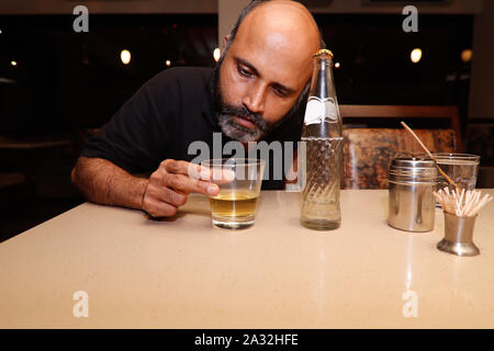 A model posing as a drunk man looking into his glaas of drink alchohol Stock Photo