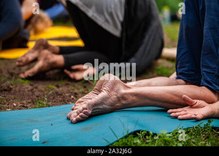 A close up view on a barefooted older person practicing yoga outside in nature with like minded people seeking enlightenment and mindfulness. Stock Photo