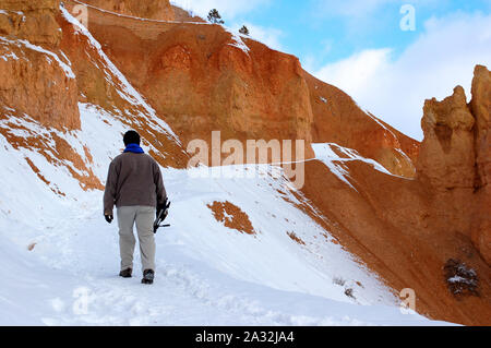 Young man hiking on snowy trail in red rocks mountain in bryce canyon Stock Photo