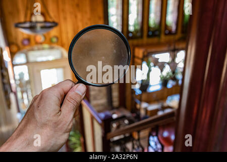 Searching inside a family home, looking through the lens of a magnifying glass in first person perspective with blurry background and copy space. Stock Photo